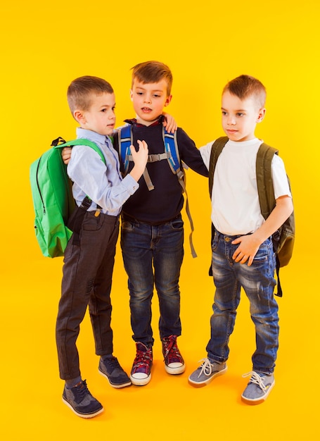 Cute schoolboys in uniform with backpacks on yellow background