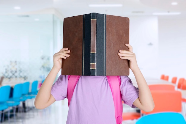 Cute schoolgirl covering her face with a book