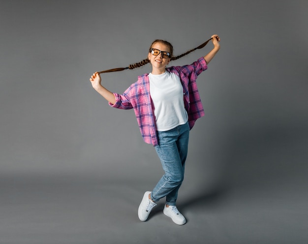 ... Cute schoolgirl. Girl with braided hair. grey background. Little girl plays with pigtails.