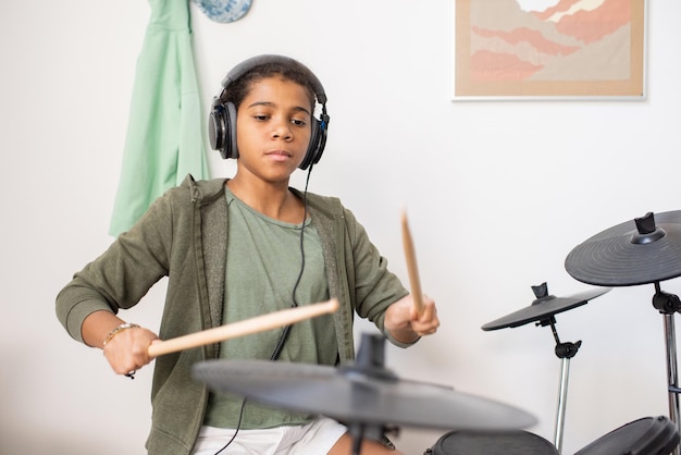 Cute schoolgirl in headphones playing drumkit