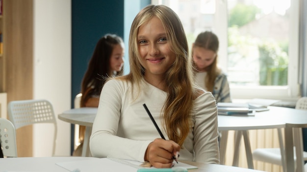 Cute schoolgirl kid girl student caucasian teen child gen z pupil learner at classroom writing task