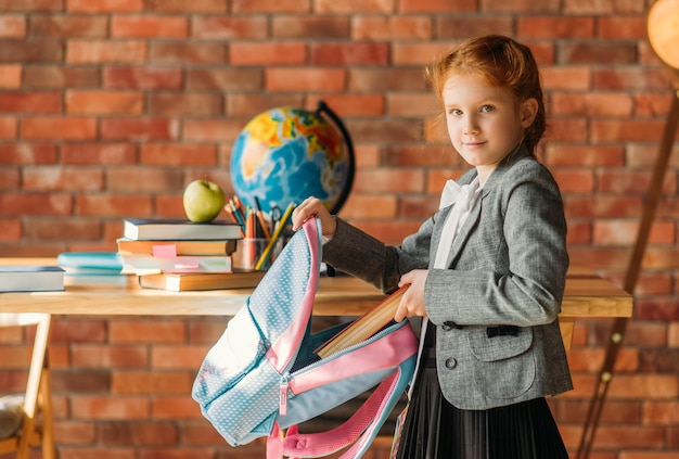 Симпатичная школьница кладет учебник в рюкзак, вид сбоку.
