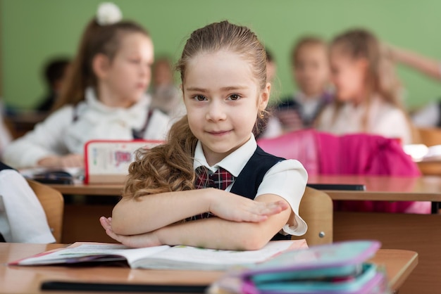 Cute schoolgirl sits at a desk with her hands clasped and smiles School