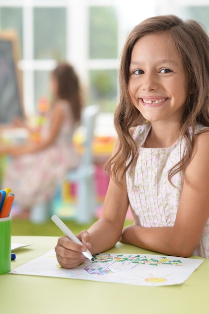 Cute schoolgirl sitting at table and drawing