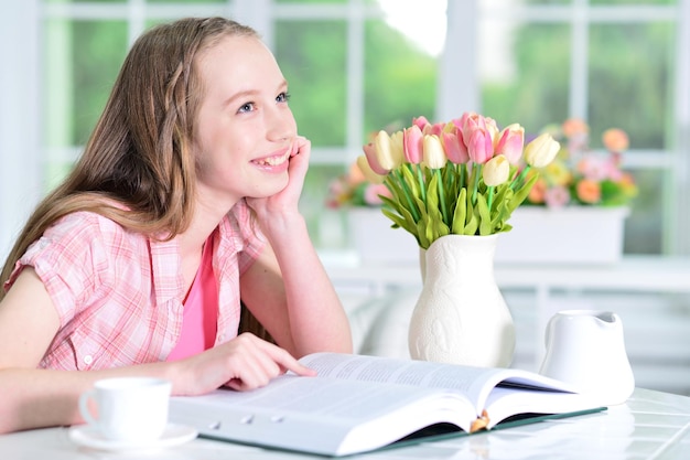 Cute schoolgirl sitting at table and reading at home