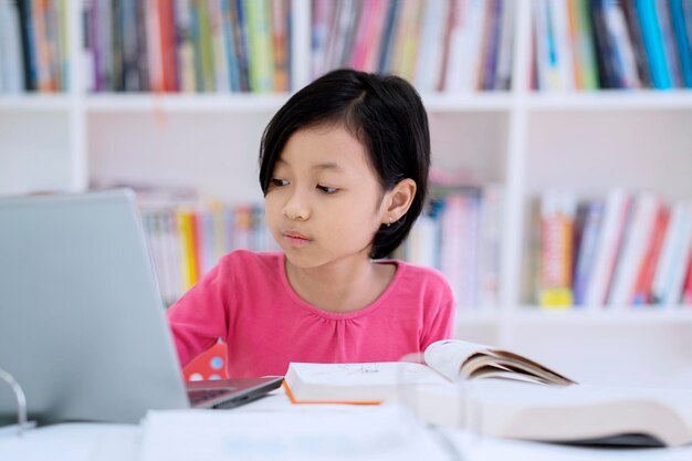 Cute schoolgirl using a laptop in the library