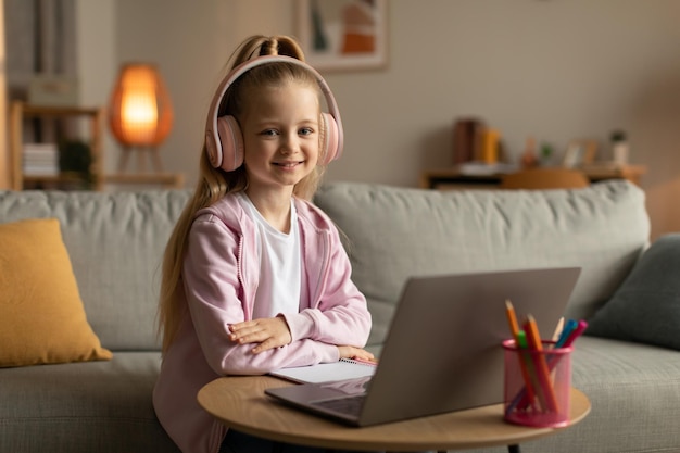 Cute Schoolgirl Using Laptop Wearing Pink Headphones Sitting At Home