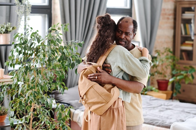 Cute schoolgirl with backpack embracing her african american grandfather