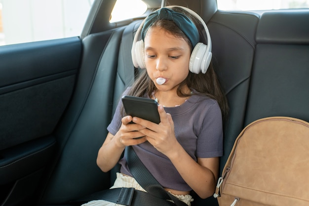 Cute schoolgirl with bubble gum scrolling in smartphone