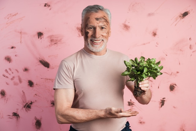 Cute, senior man on a wall of a dirty pink wall holding a basil