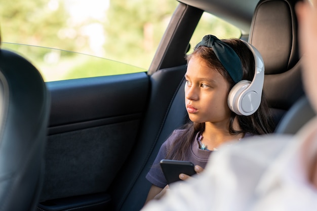 Cute serious girl with headphones scrolling in smartphone