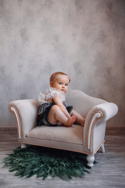 Cute serious newborn baby sitting on sofa. Infant girl sitting on special little baby furniture