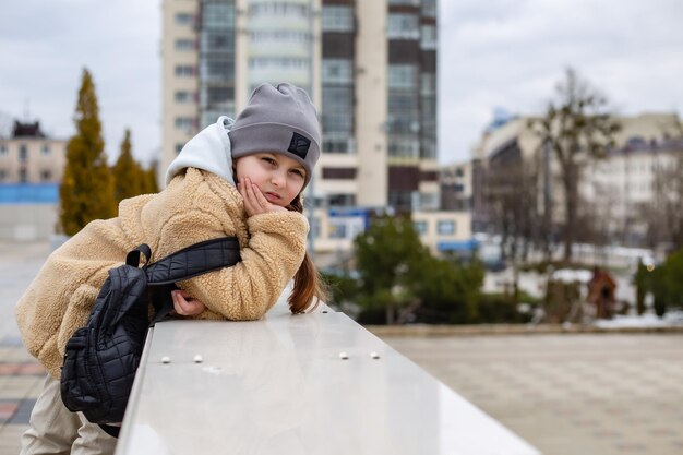 a cute sevenyearold girl in a faux fur coat stands near the parapet in the city