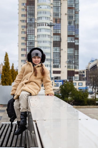 彼女の手にバックパックを持ったかわいい7歳の女の子が街の欄干に座っています