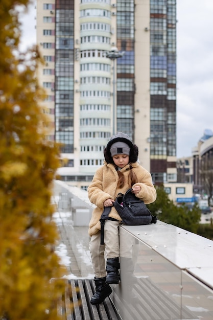 彼女の手にバックパックを持ったかわいい7歳の女の子が街の欄干に座っています