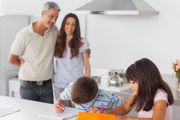 Cute siblings drawing together in kitchen with their parents smiling 