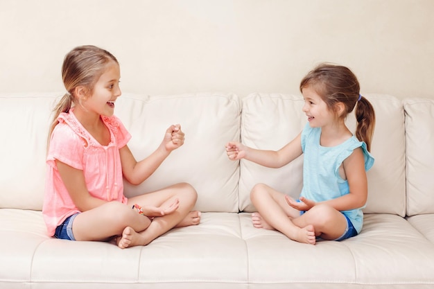 Photo cute sisters playing while sitting on sofa at home