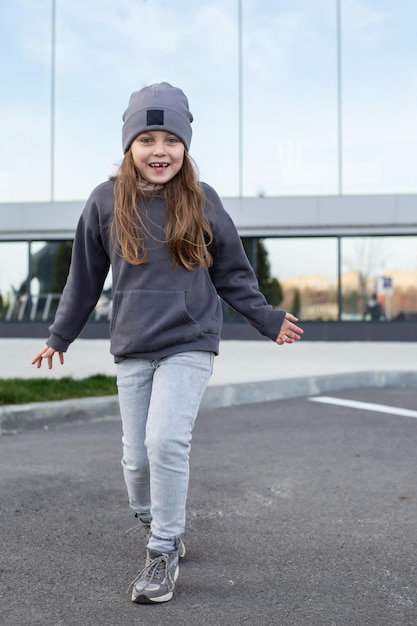 a cute six years old girl in jeans and a gray hoodie walks and smiles broadly