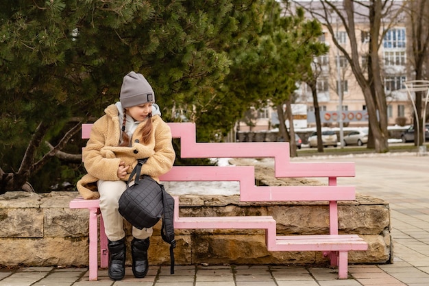 環境にやさしいフェイクファーで作られたベージュの毛皮のコートを着たかわいい6歳の女の子がベンチに座っています