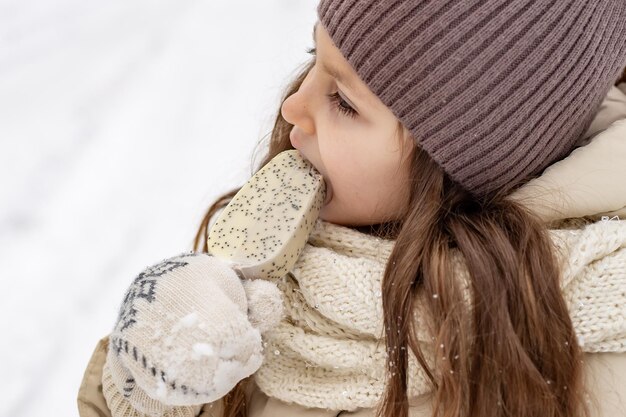 a cute sixyearold girl eats popsicle ice cream with pleasure in the winter in the forest