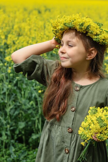 a cute sixyearold girl stands in a rapeseed field with a wreath of rapeseed flowers on her head