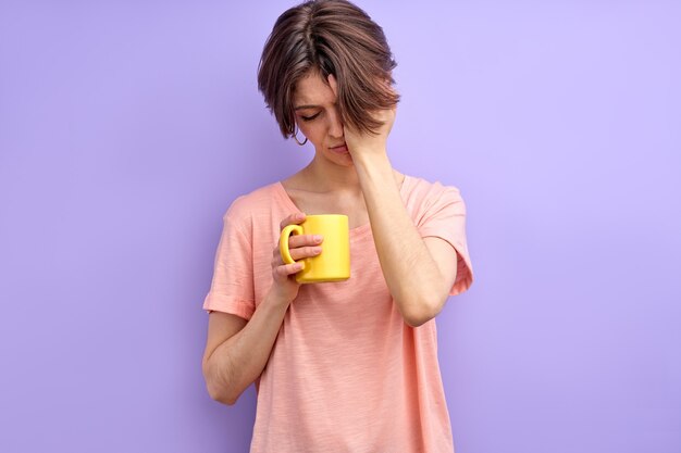 Cute sleepy woman having no enough sleep holding yellow mug in hands coffee in the morning adult wom...