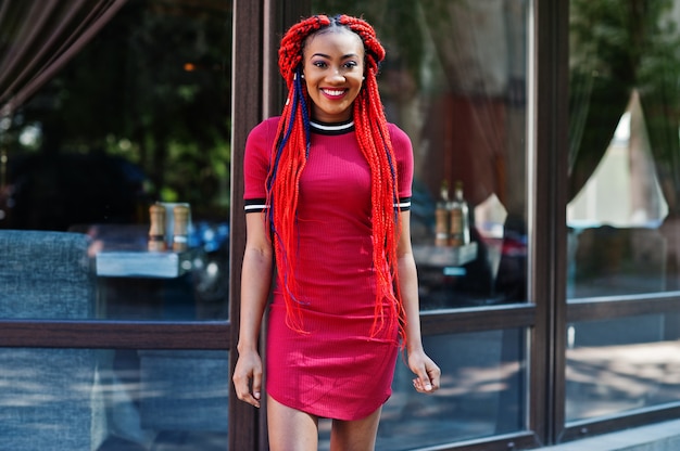 Cute and slim woman in red dress with dreadlocks and backpack posed outdoor on street