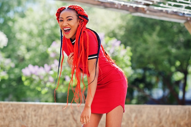 Cute and slim woman in red dress with dreadlocks in motion having fun on street