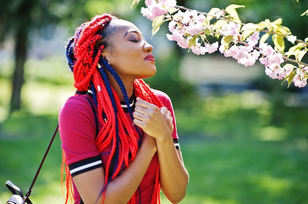 春の公園で屋外ポーズドレッドヘアを持つ赤いドレスのキュートでスリムな女性
