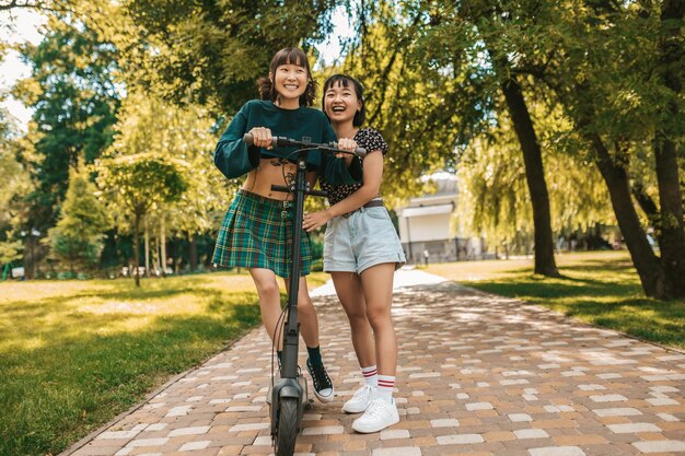 Cute slim young girls riding a scooter in the park