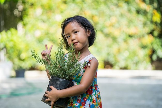 Cute small girl holding rosemary plant standing in garden