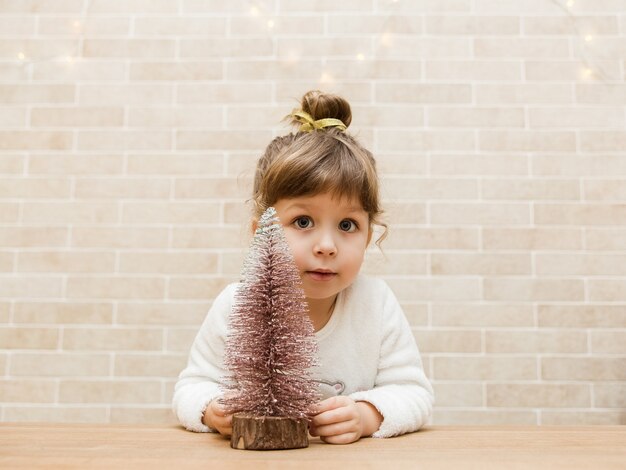 Cute small girl with Christmas treeBrick wall backgroundMinimalist style