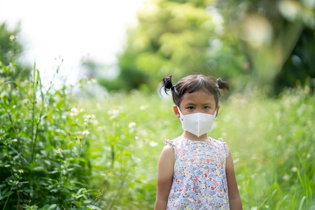 Cute small girl with protective face mask standing at field