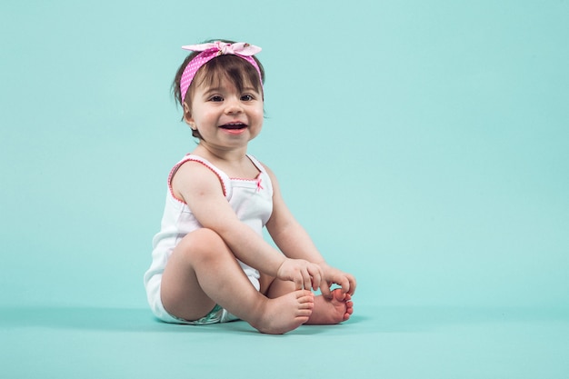 Cute small smiling girl with pink bow in hair sitting in studio posing  blue  