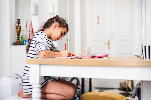 Cute smart primary school child girl learning writing doing homework sit at home table