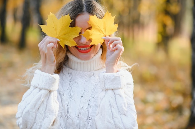 自然​の​中​で​紅葉​を​保持している​かわいい​笑顔​の​女性​。