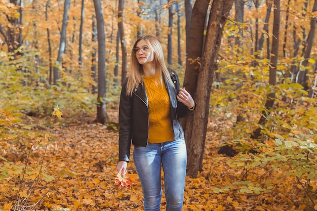 Cute smiley woman holding autumn leaves in fall park seasonal lifestyle and leisure concept