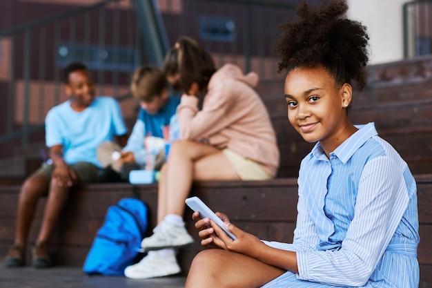 Cute smiling African American schoolgirl with mobile phone