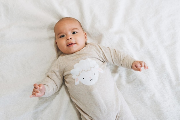 Cute smiling baby boy 46 month in beige overall on the bed natural tones