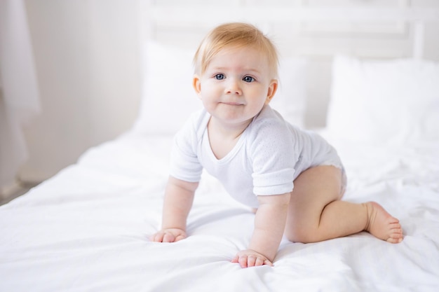 Foto un bambino sorridente e carino impara a strisciare su un letto bianco a casa un bambino biondo si sveglia al mattino felice infanzia e famiglia