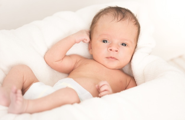 Cute smiling baby boy lying on soft beige blanket and cushion