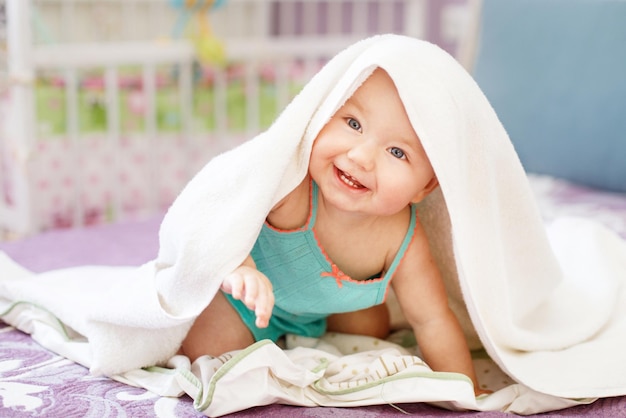 Милый улыбающийся ребенок смотрит в камеру под белым полотенцем портрет милого ребенка
