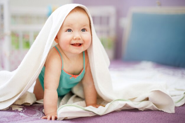 Cute smiling baby looking  under a white towel on a white background