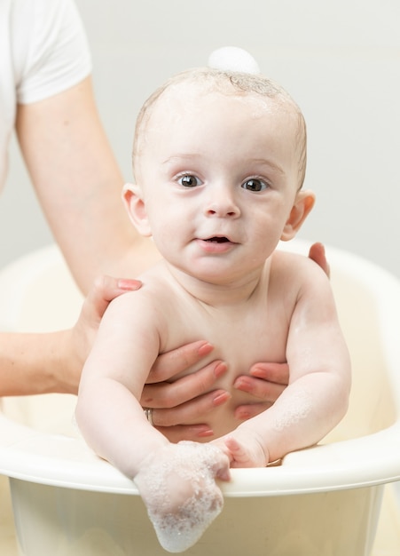 Cute smiling baby sitting in bath and looking at camera