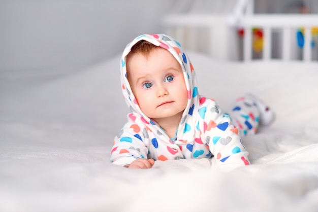 Cute smiling baby in a stylish hoodie lying on a white blanket