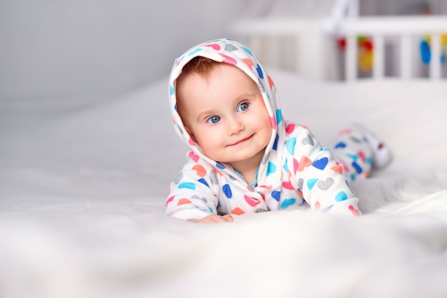 Bambino sorridente sveglio in una felpa con cappuccio alla moda che si trova su una coperta bianca