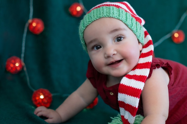 新年の背景に飾られたクリスマスの帽子をかぶってかわいい笑顔の赤ちゃん。赤、緑、白の色