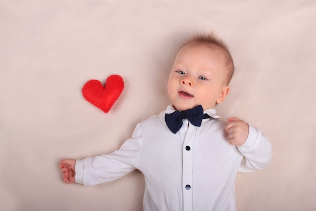 Cute smiling baby wearing tuxedo with red toy heart