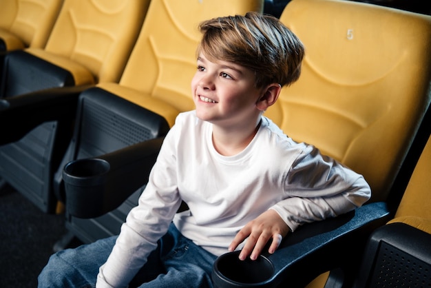 Симпатичный улыбающийся мальчик сидит в кино и смотрит фильм