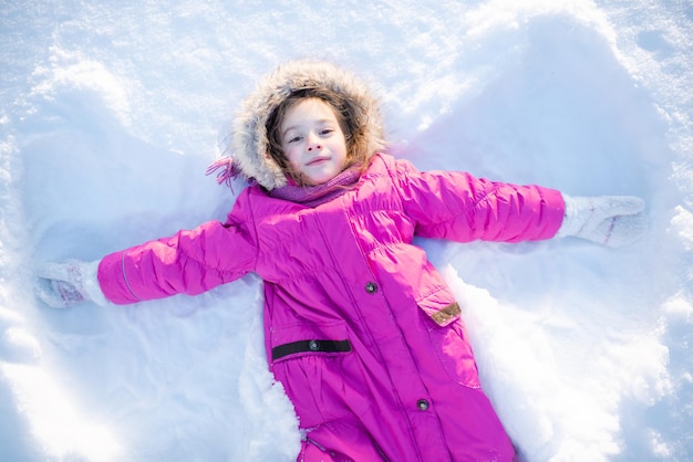 写真 かわいい笑顔の子供の女の子 56 歳の雪の中で横になっている天使の形を作る屋外冬の休日の季節の幸福